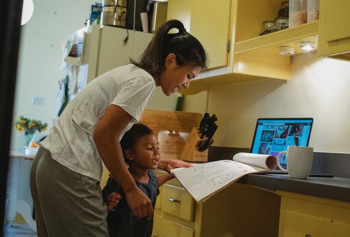 Delighted young Asian mother and little daughter doing homework together in kitchen